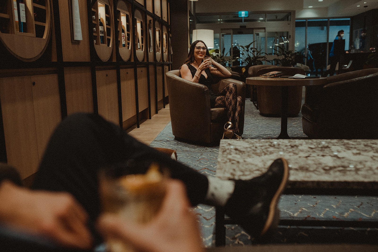 Photo of a stunning woman sitting in a chair in a hotel lobby looking over at her partner from afar
