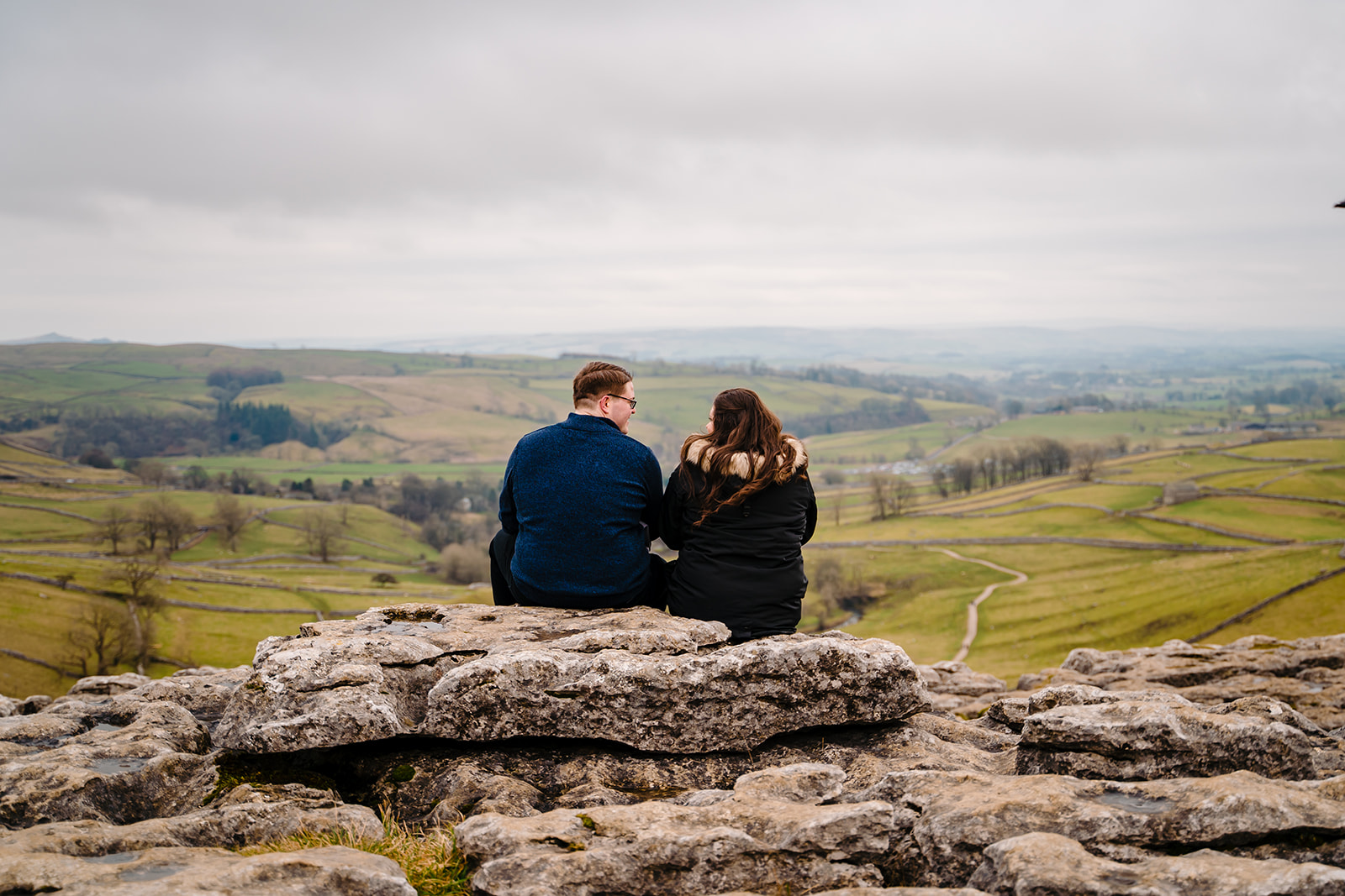Couple is sat at the top of Malham Cove 
