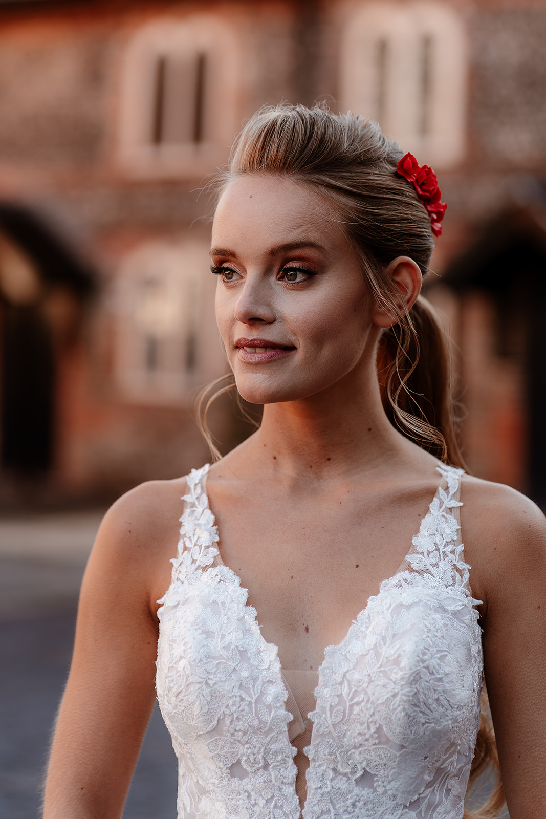 Close up of a bride in a white lace wedding dress with red flowers in her hair. 