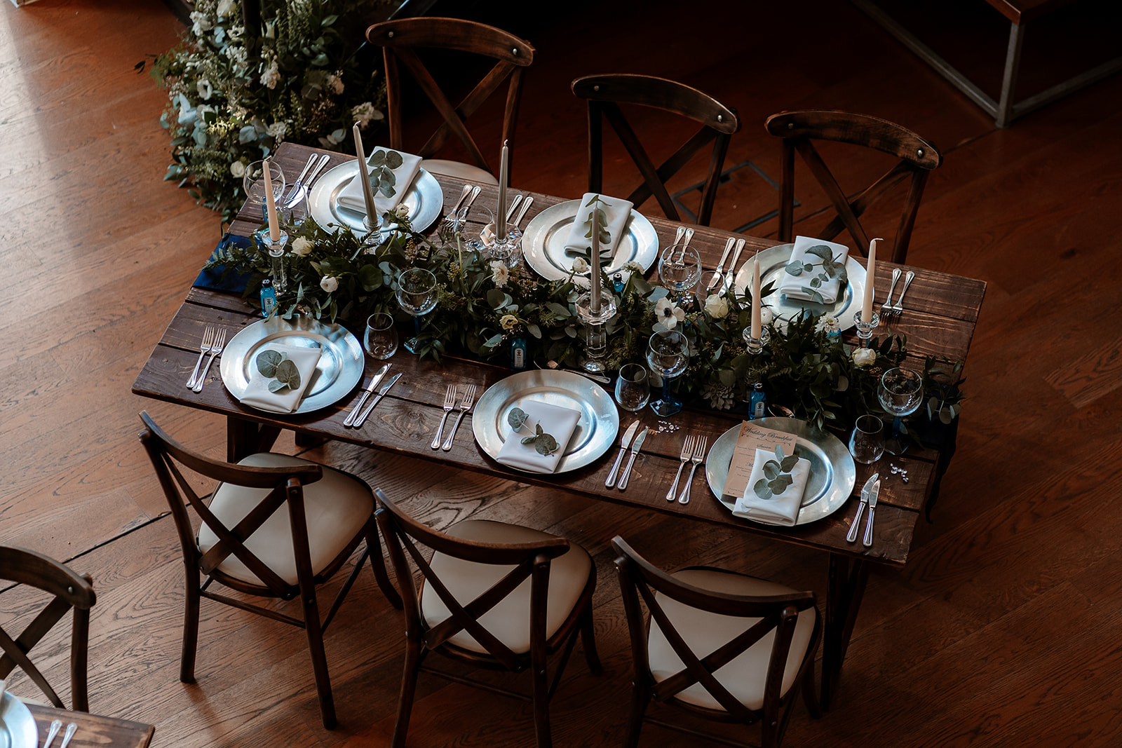Wedding breakfast tables with green and white flower table runners and tapered candles at the Bombay Sapphire Distillery