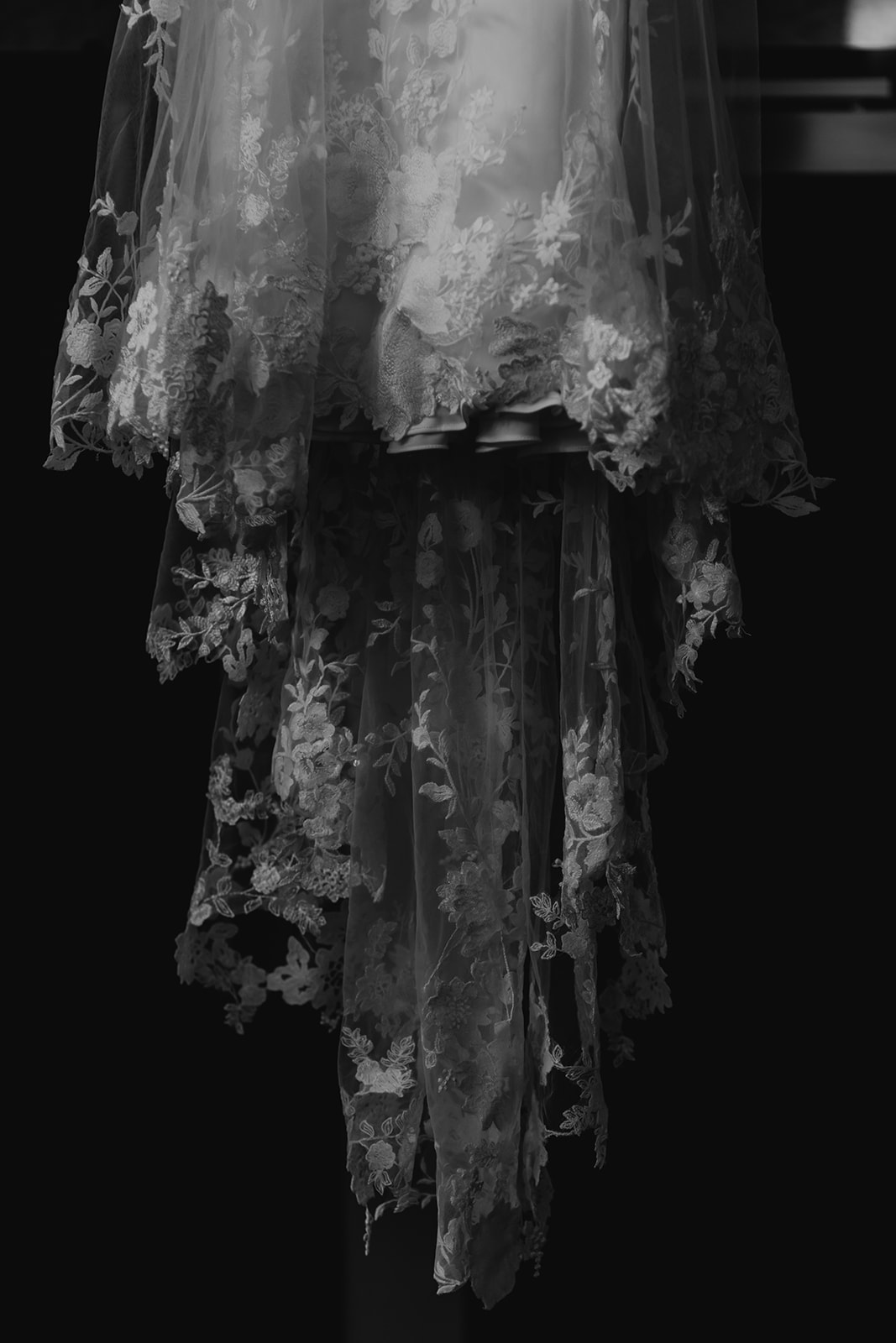 Black and white image of the lace train of a wedding dress hanging from a staircase. 