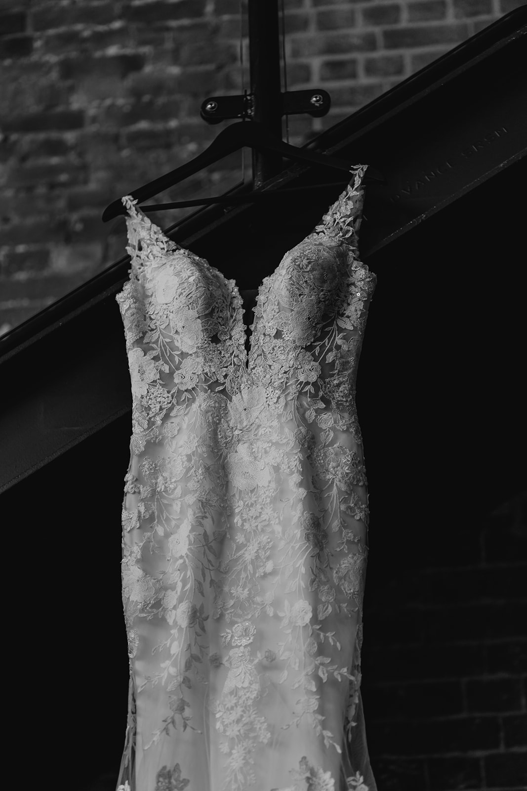 Black and white image of a lace wedding dress hanging from a staircase at the Bombay Sapphire Distillery. 