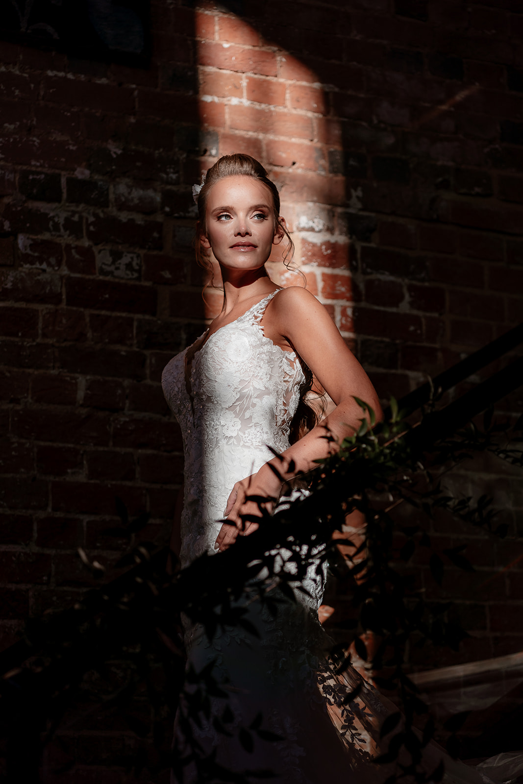 Bride stands in a shaft of light on a staircase at the Bombay Sapphire Distillery.