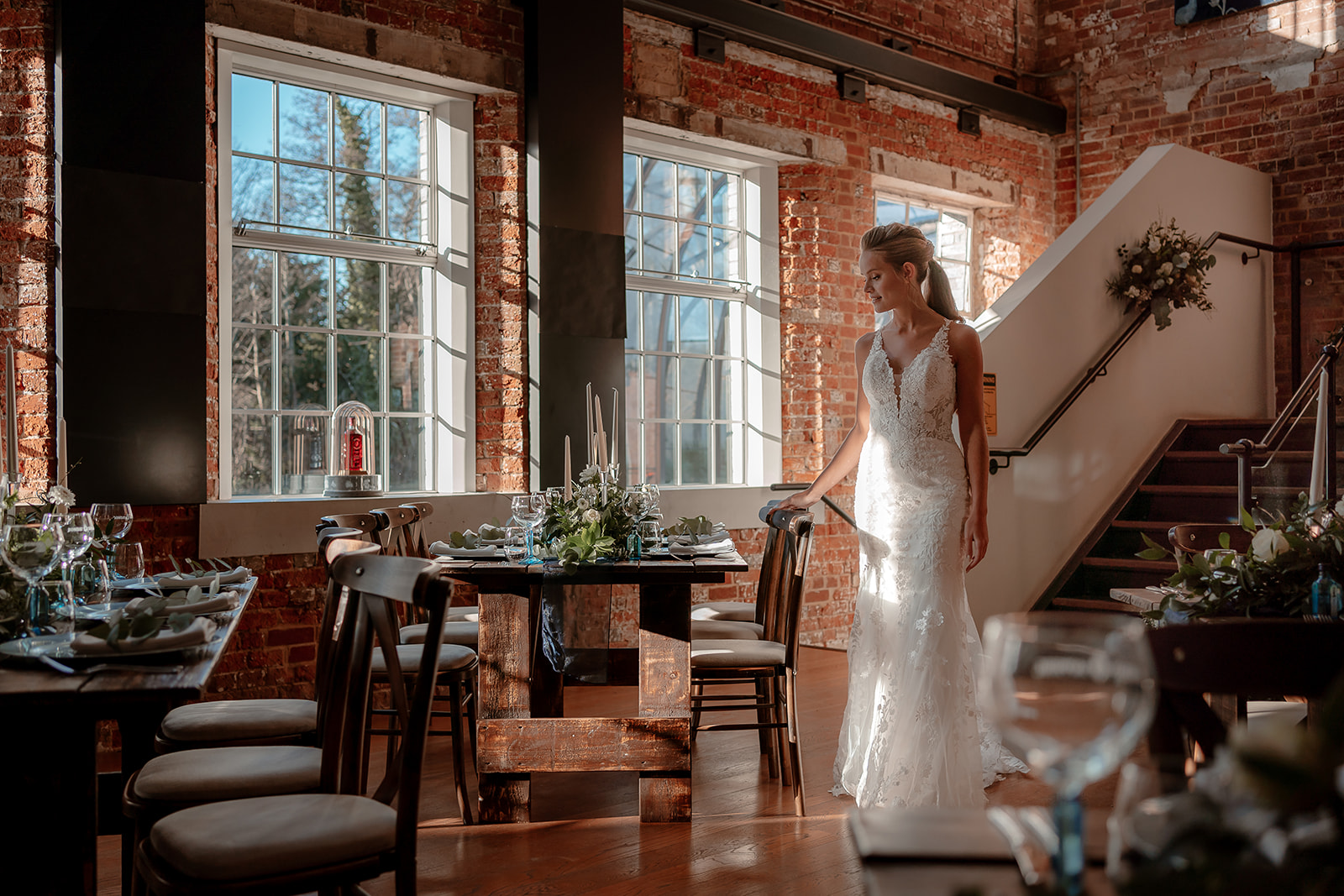 A bride in a white lace fit and flare dress walks between tables in the wedding reception room at Bombay Sapphire