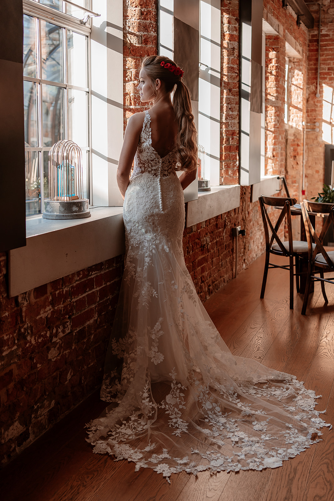 Bride in a white lace dress stands and looks out the window at the Bombay Sapphire Distillery.