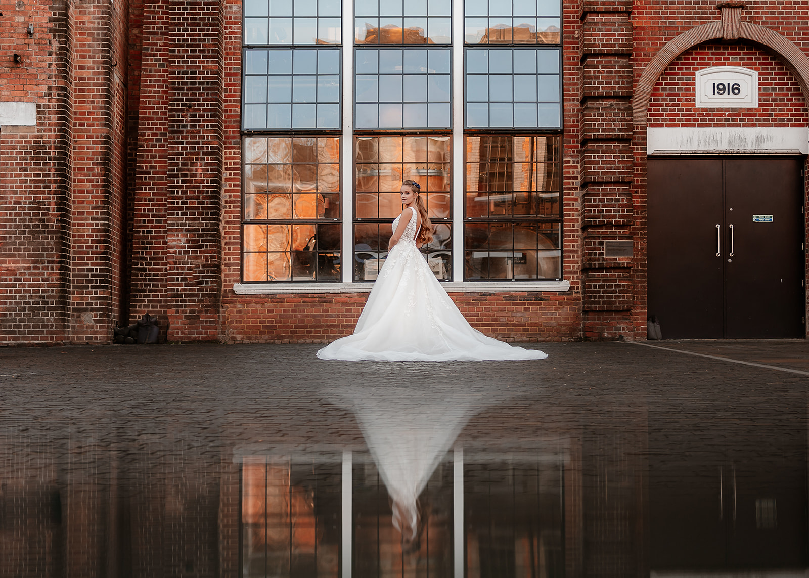 Bridal model in a white wedding dress stands in front of tall industrial windows at the Bombay Sapphire Distillery. 