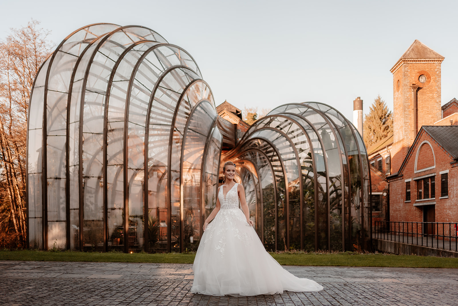 Bride in a white wedding dress stands in front of the Bombay Sapphire Distillery Glasshouses. They frame her like wings.