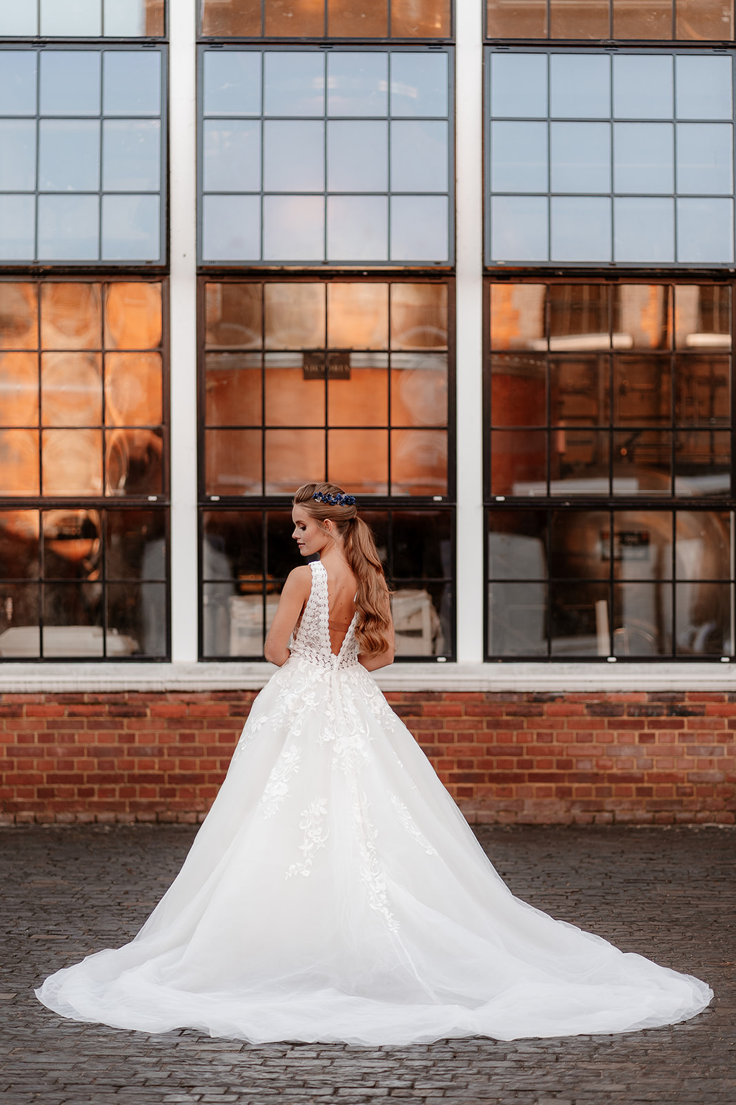Bridal model in a white ballgown dress stands in front of tall industrial windows at the Bombay Sapphire Distillery. 