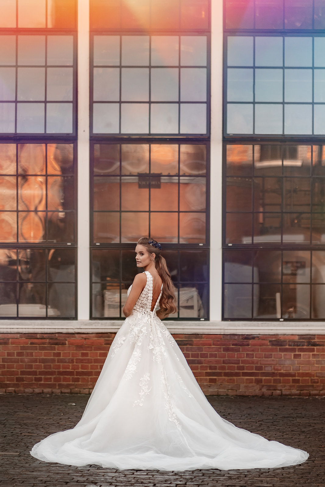 Bridal model in a white princess dress stands in front of tall industrial windows at the Bombay Sapphire Distillery. 