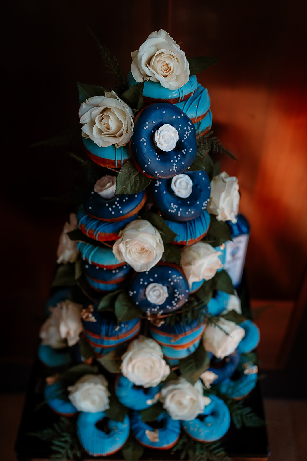 A tower of ring doughnuts decorated with blue icing and white roses. 