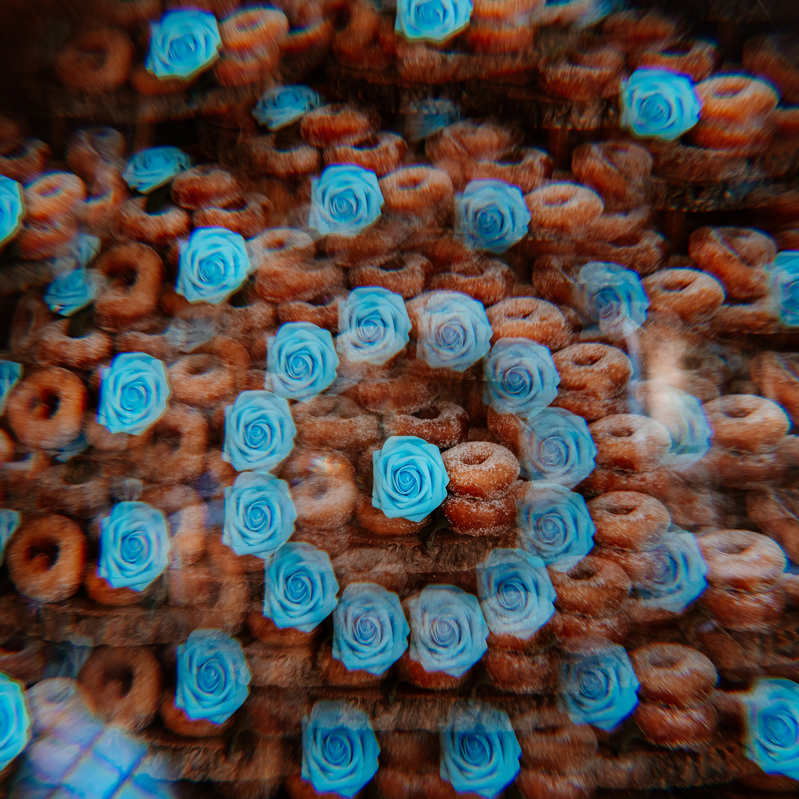 A kaleidoscope image of sugar covered ring doughnuts decorated with blue icing sugar roses.