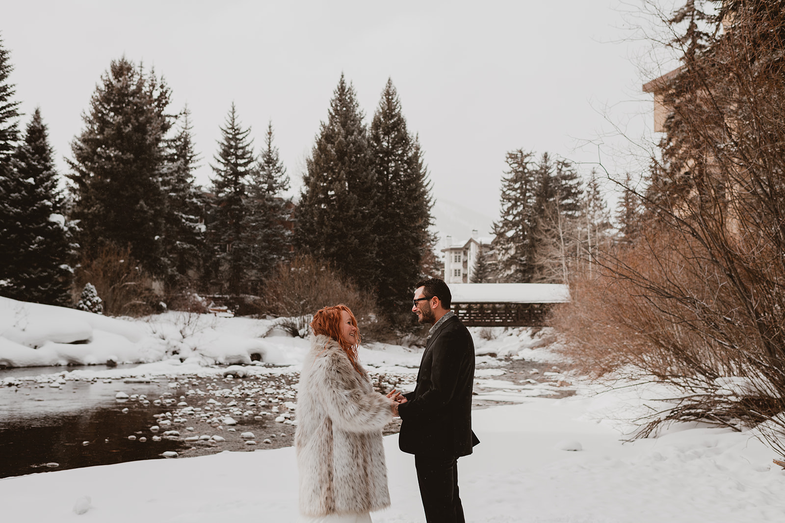 Couple getting married, standing by a river in the snow of Vail Village in front of the covered bridge 