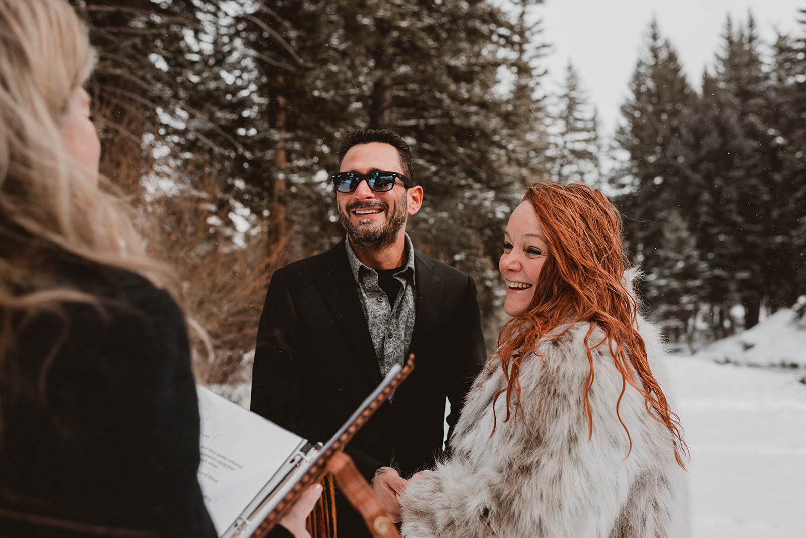 Couple laughs as they exchange vows in the winter landscape, holding hands to keep warm in Vail Colorado 
