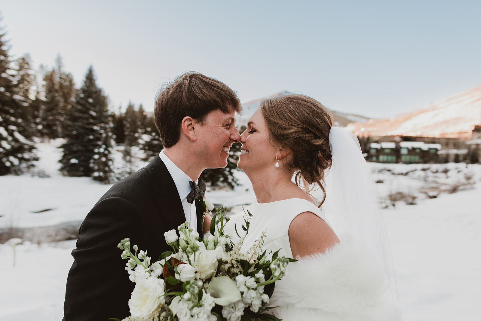 Couple laughing in their wedding attire outside in the snow in Vail, Colorado with the mountains behind them 