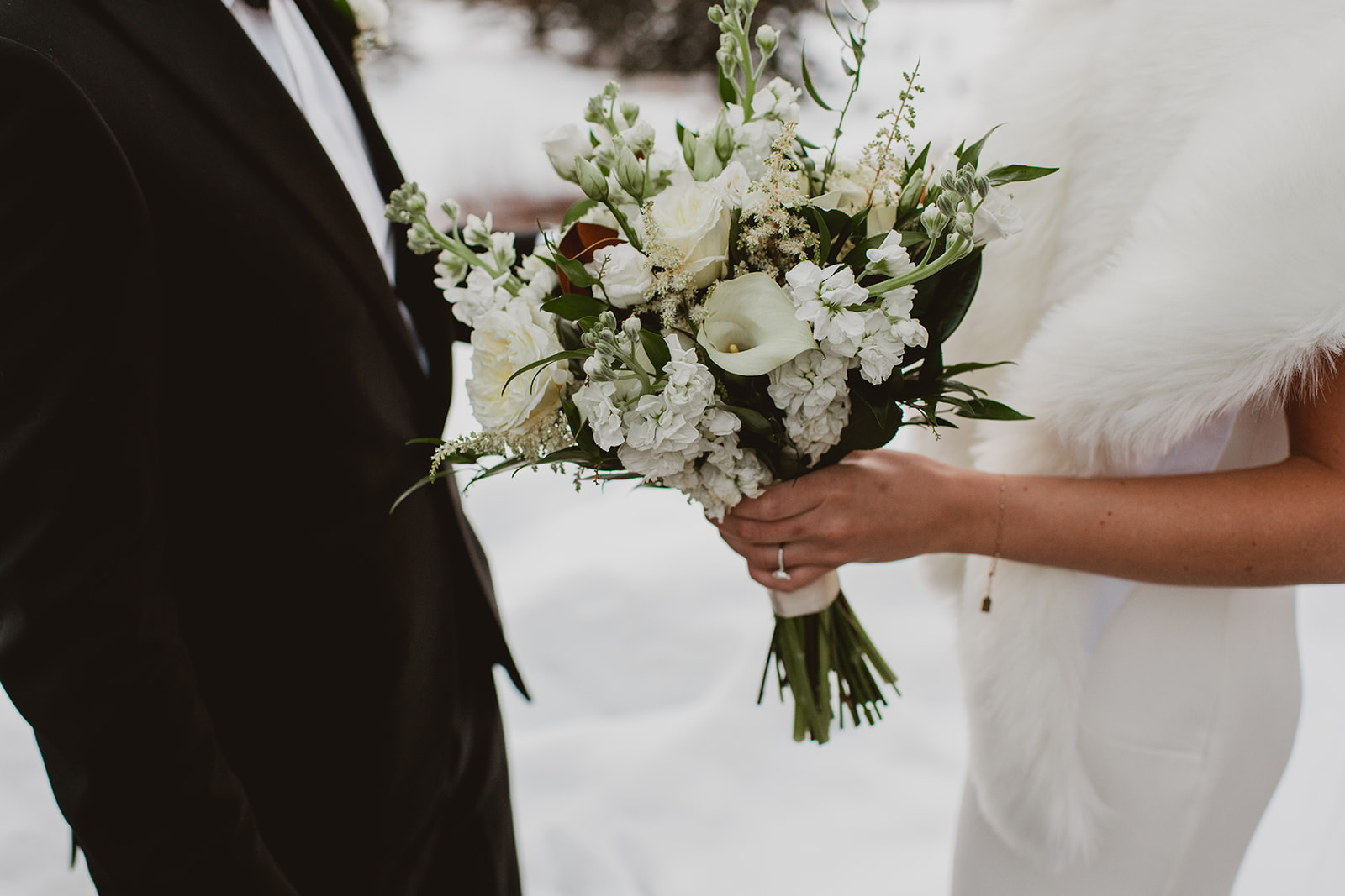 White and green wedding bouquet in brides hand surrounded by snow in Vail, Colorado 