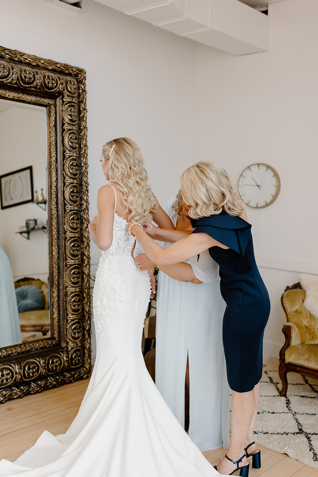 Bride gets into her wedding dress on her wedding day while her mom and sister zip her up. 