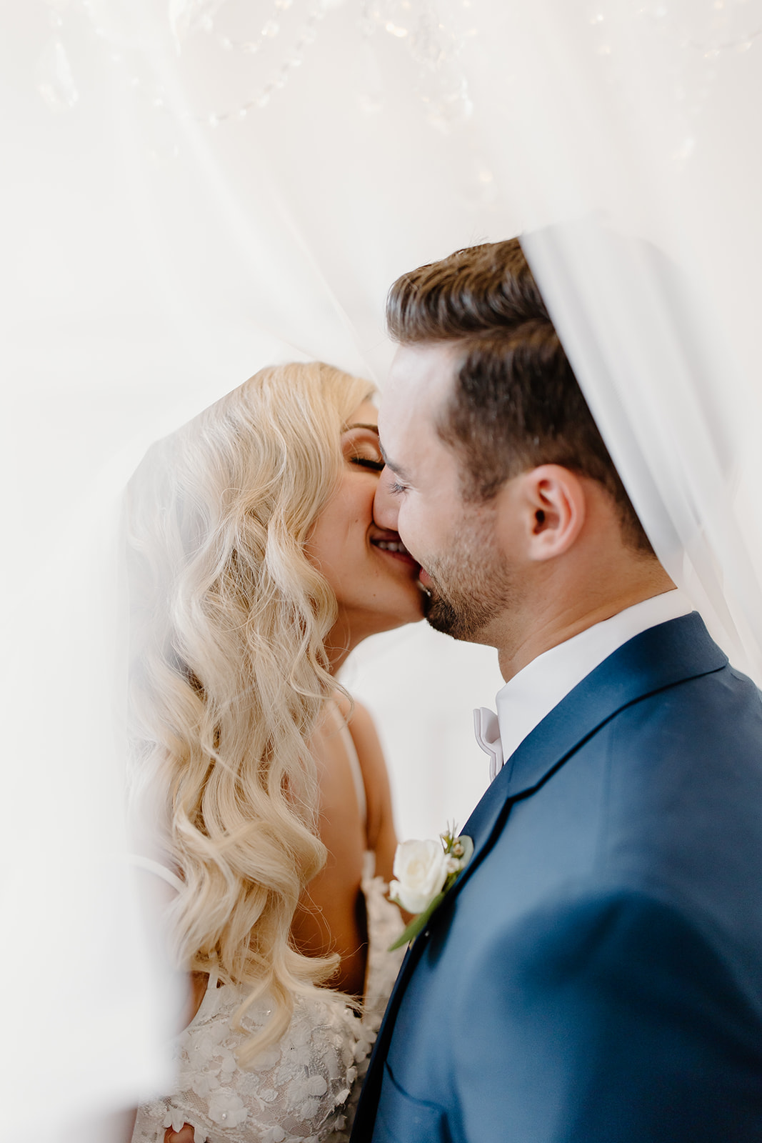 Bride and groom kissing underneath the bride's veil.