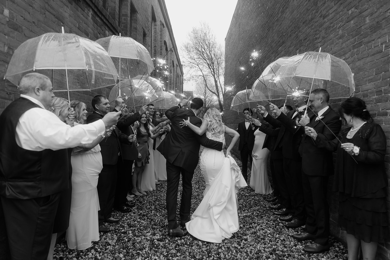 Bride and groom run while all of their family and bridal party hold sparklers and umbrellas. 