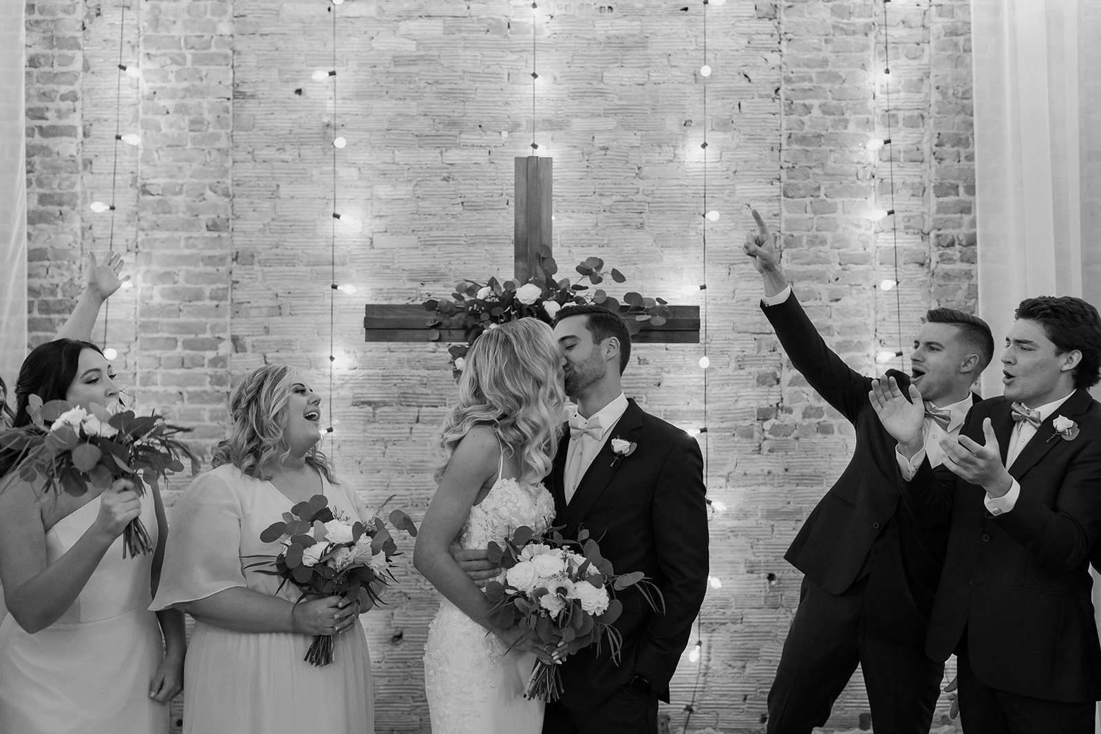 Bride and groom share a kiss as all of their bridesmaids and groomsmen cheer.
