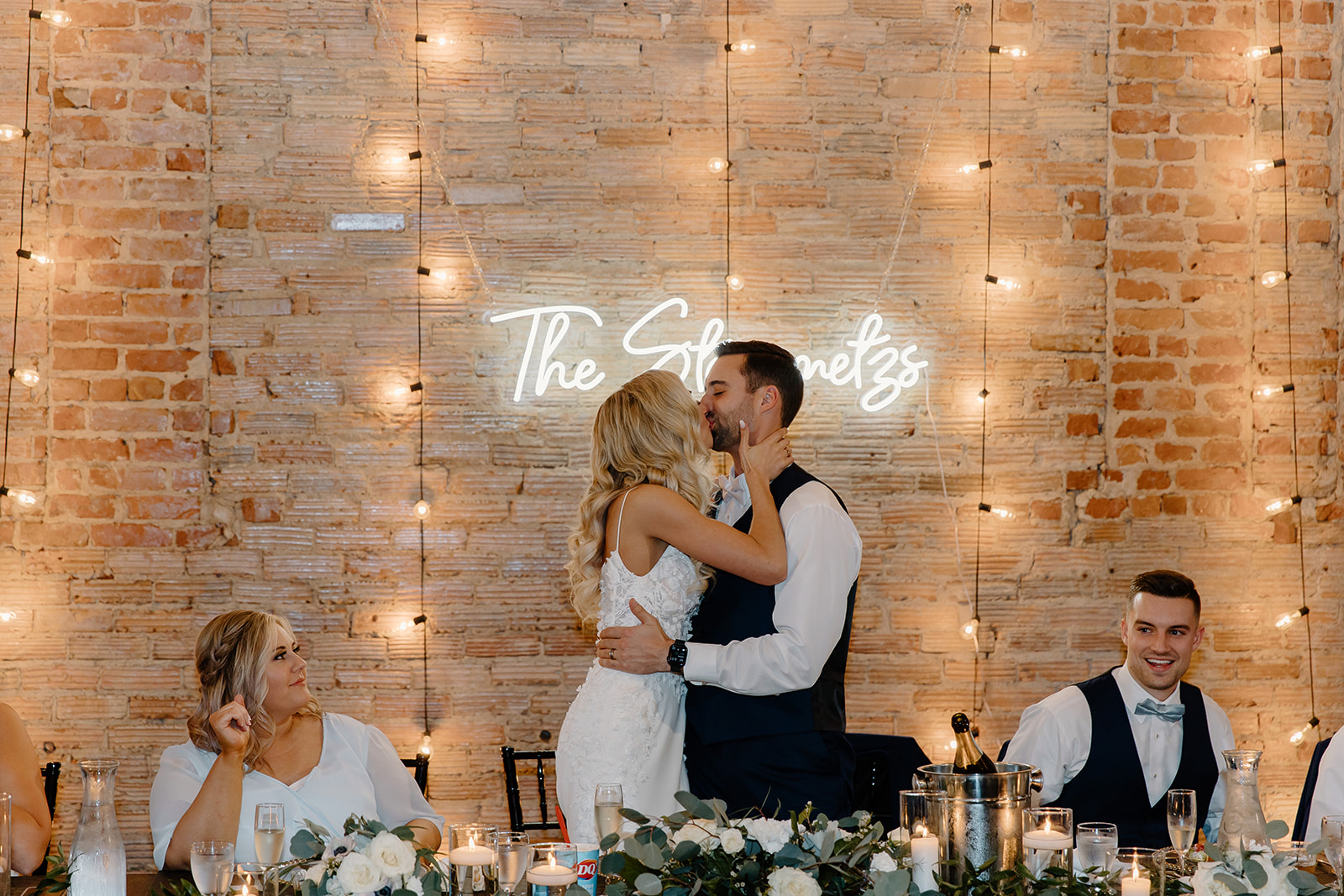 Bride and groom share a kiss in front of their neon sign on their wedding day.