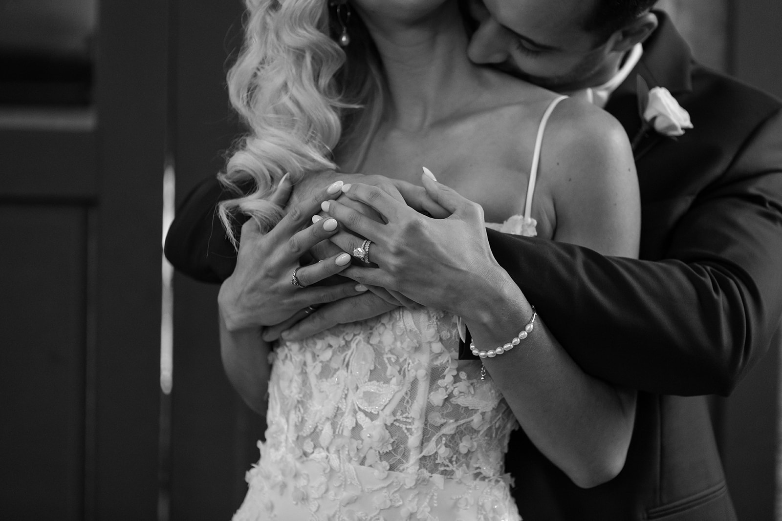 Bride and groom's hands together while groom kisses her shoulder.