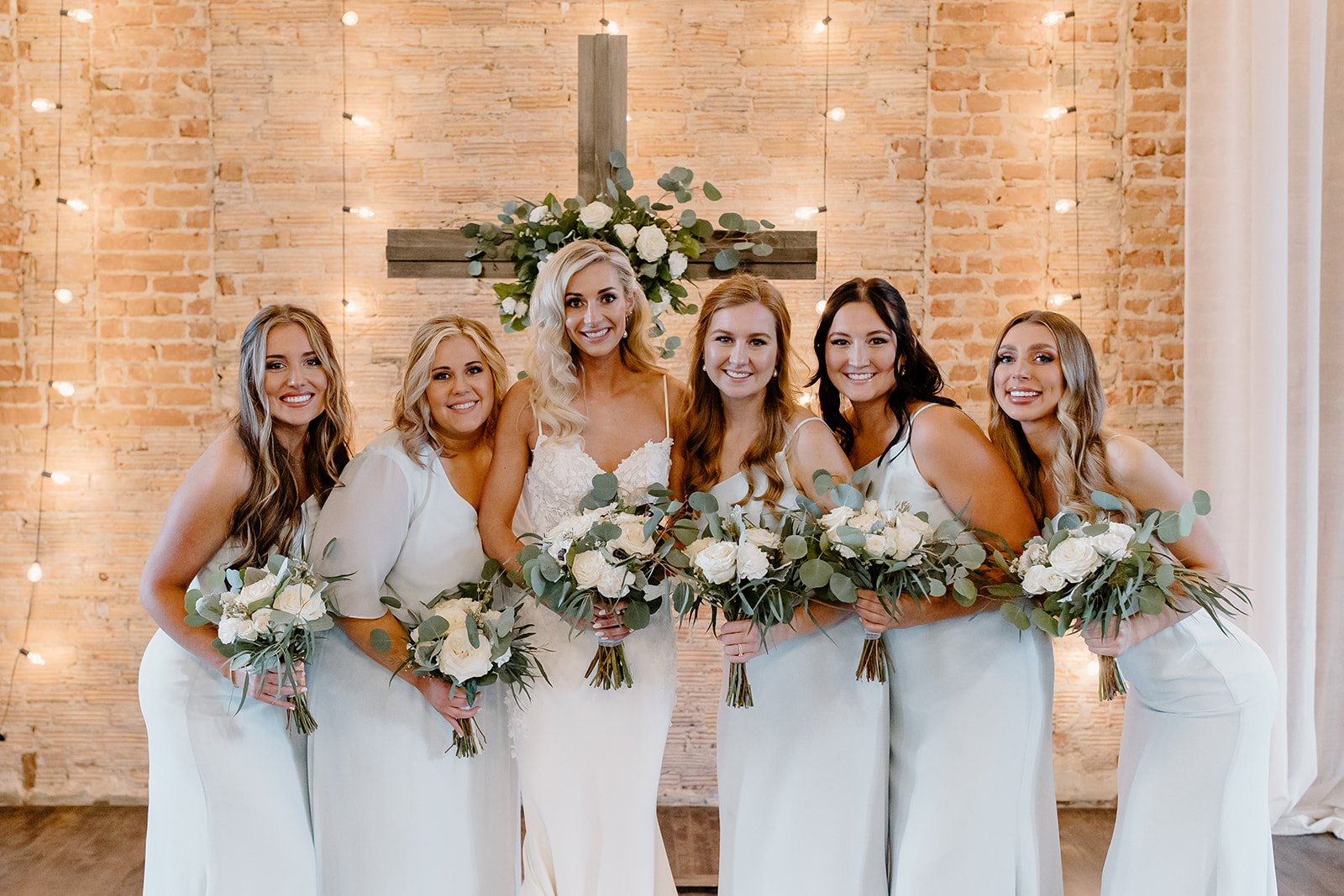 Bride and her bridesmaids pose in front of a cross. 