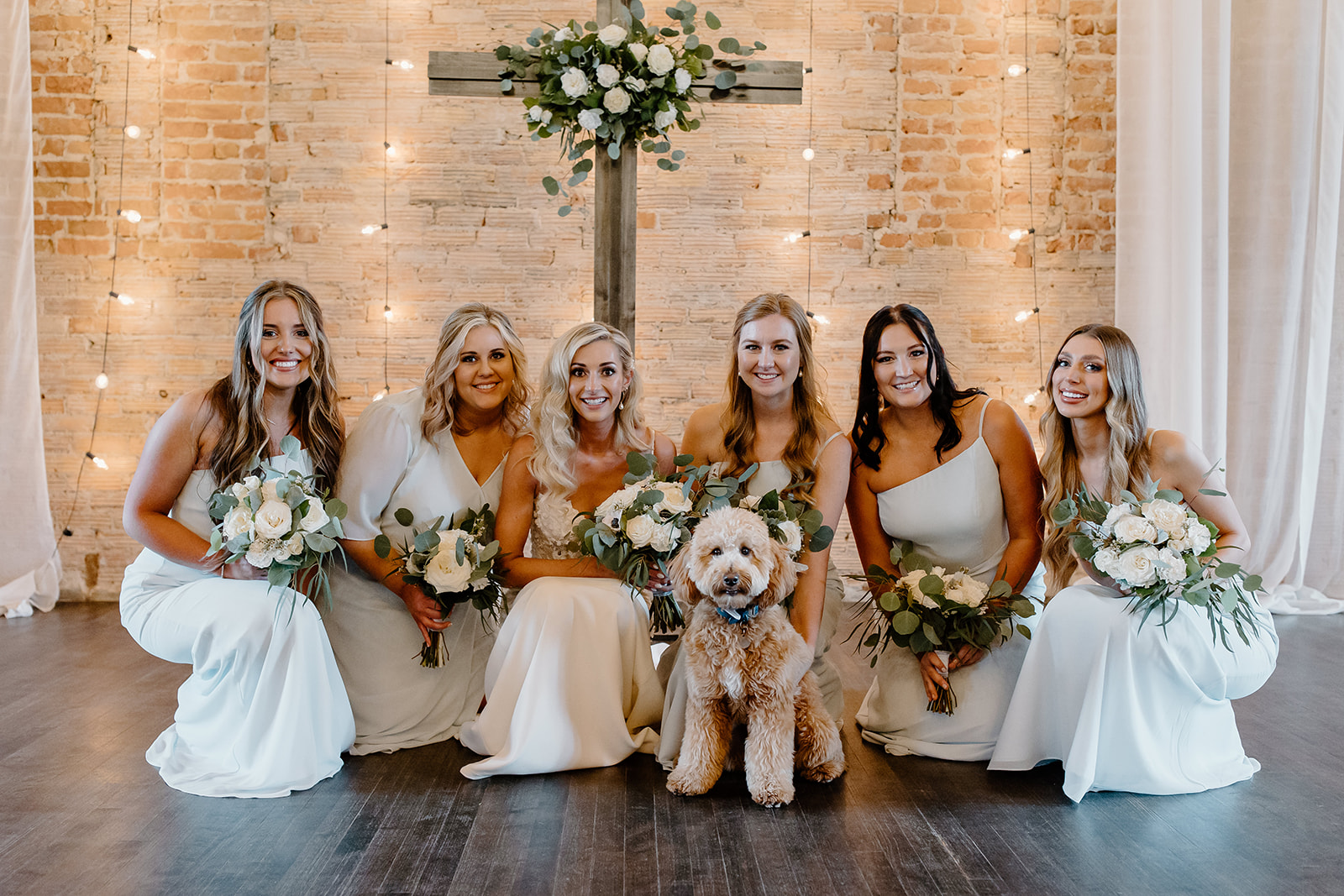 Bride, her dog, and her bridesmaids pose in front of a cross. 