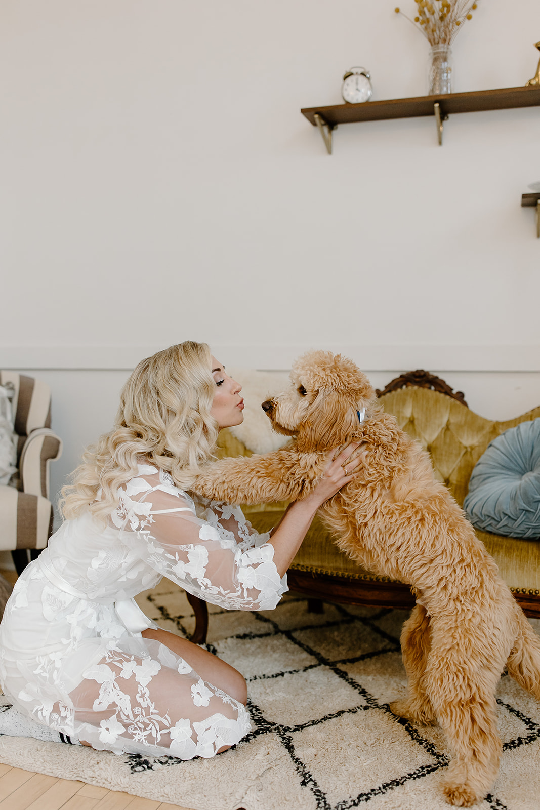 Bride kneels on the floor with her mini golden doodle and gives him a kiss.