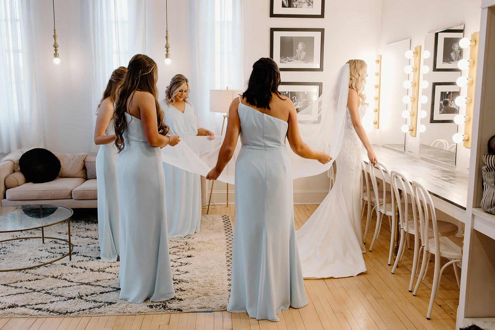 Bride looks in a mirror while all of her bridesmaids surround her and hold her veil.
