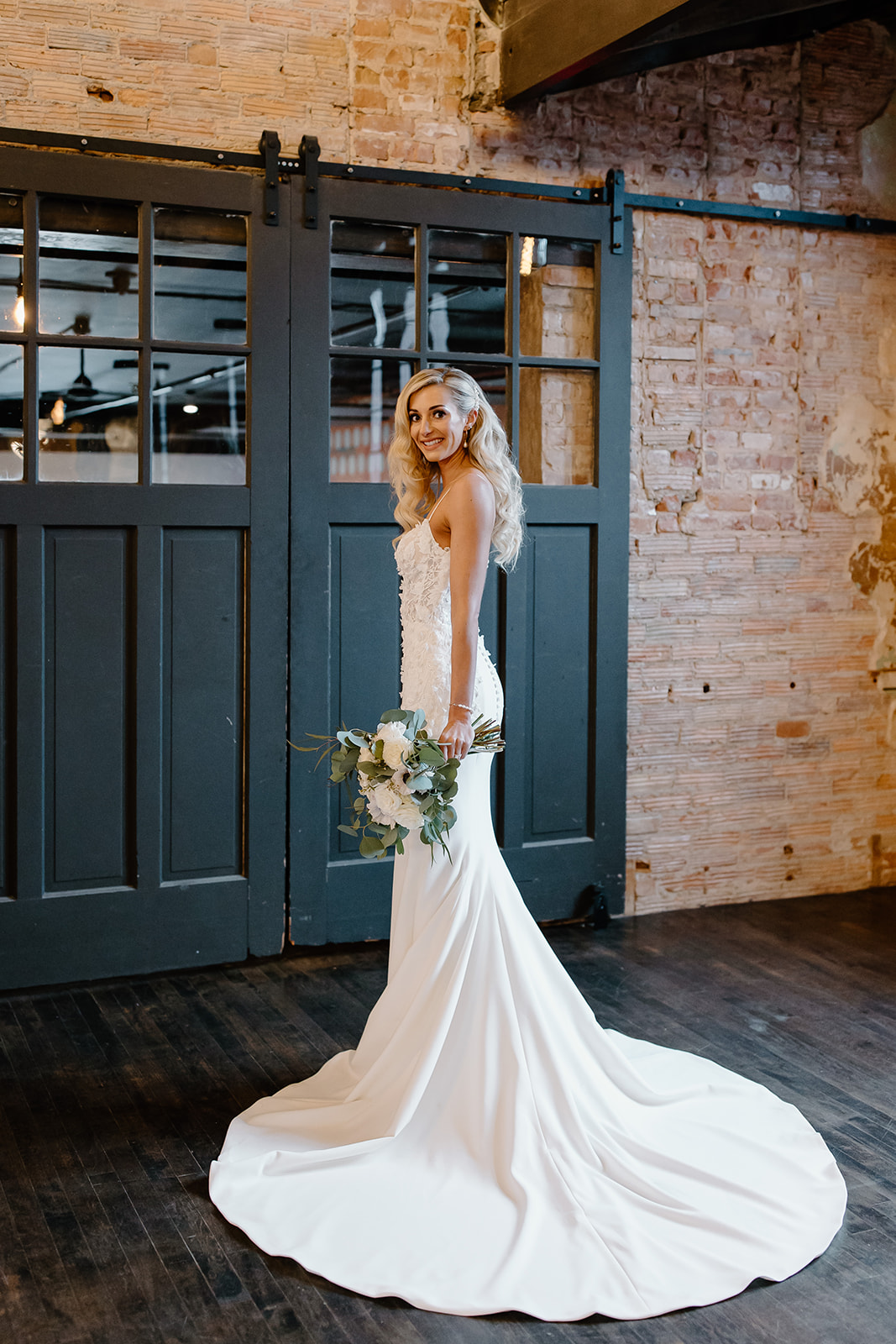 Bride looks over shoulder while holding her bouquet showing off the train of her wedding dress. 