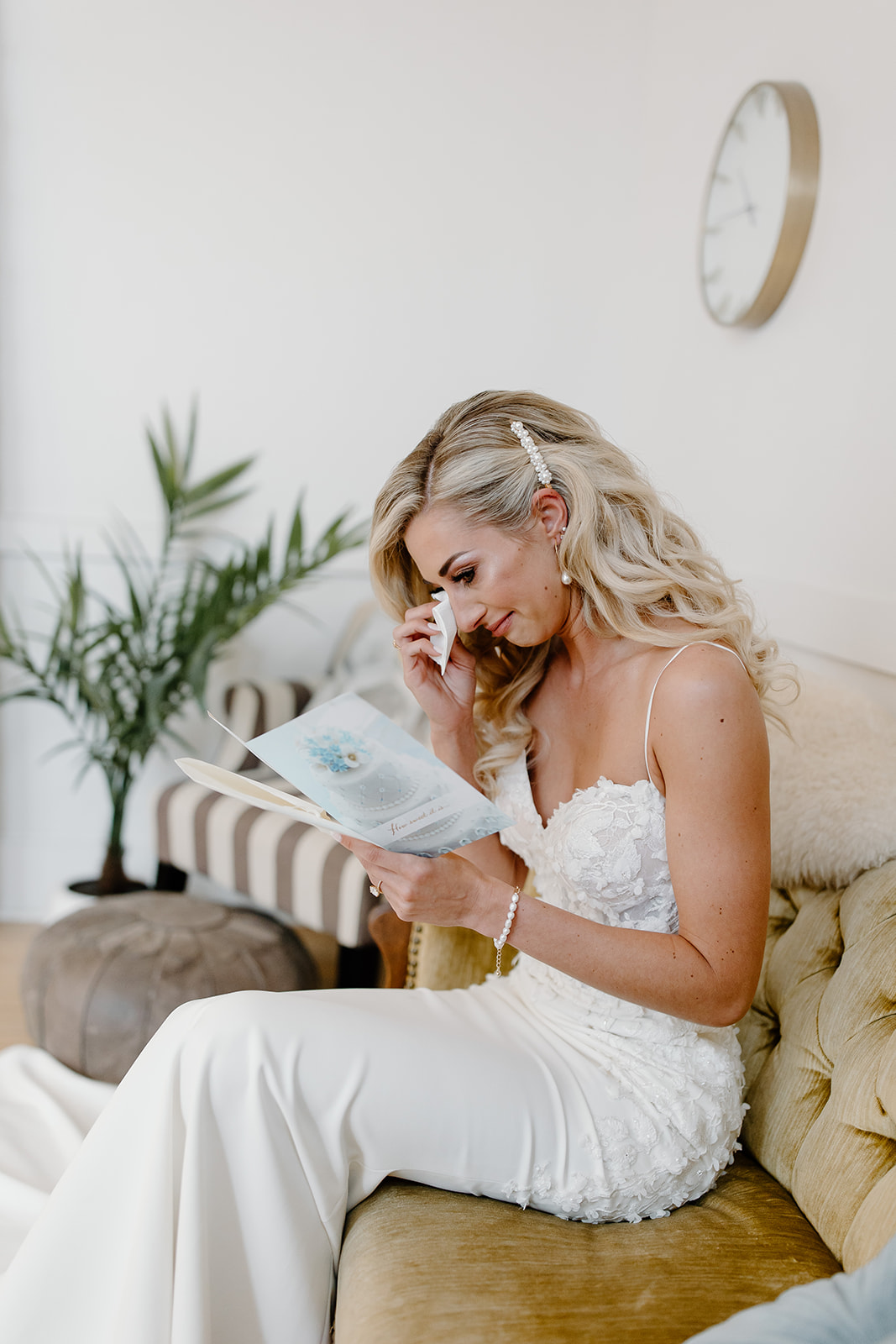Bride sits on vintage couch as she cries reading a letter from her groom.