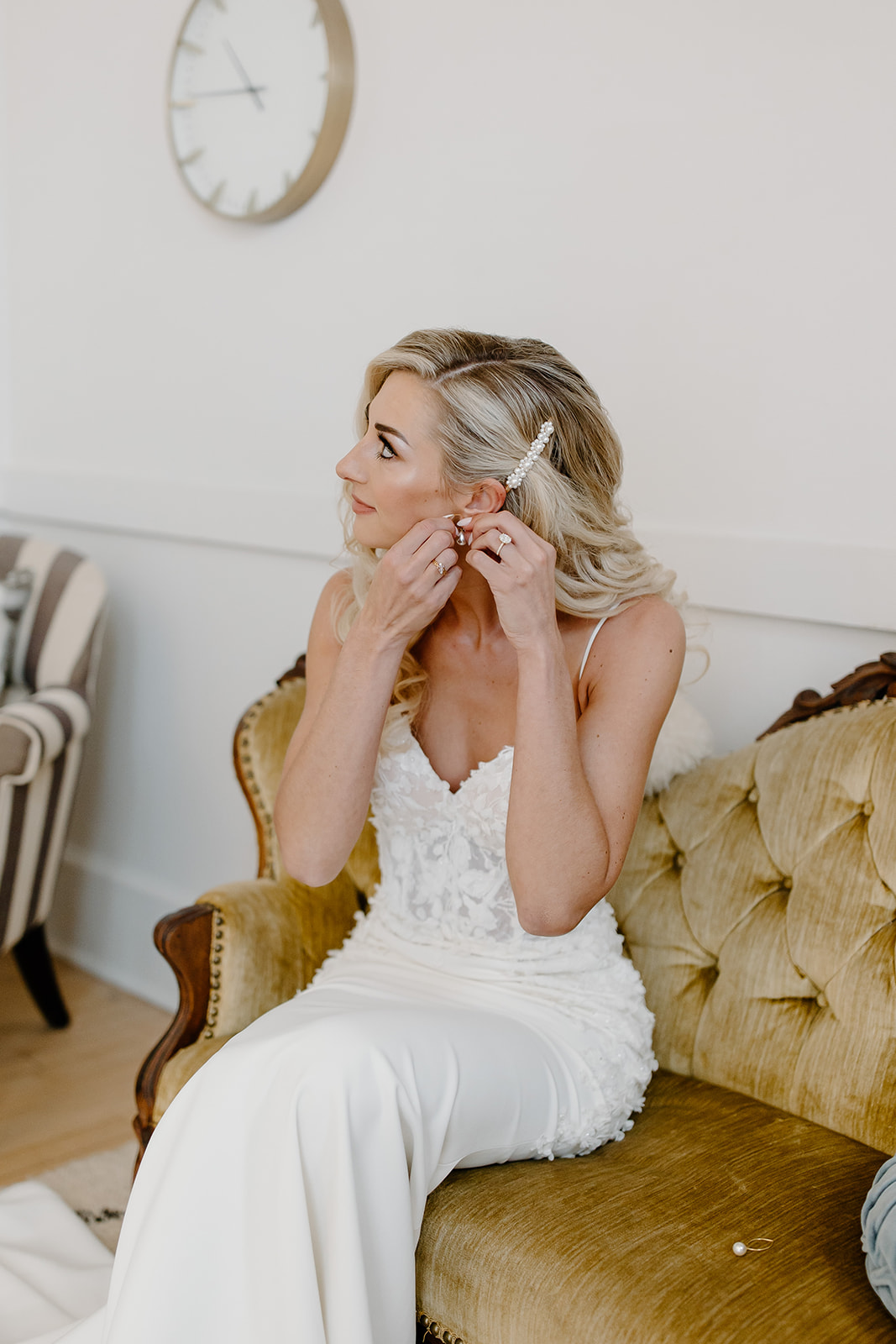 Bride sits on vintage couch as she puts her earrings in.