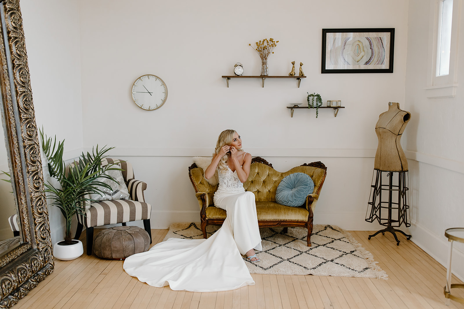 Bride sits on vintage couch as she puts her earrings in.