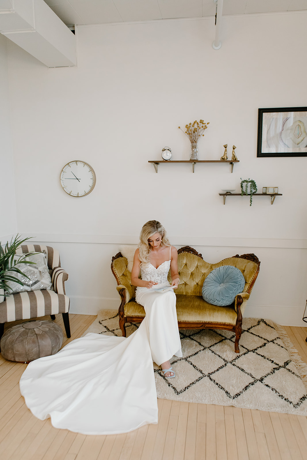 Bride sits on vintage couch as she reads a letter from her groom on their wedding day.