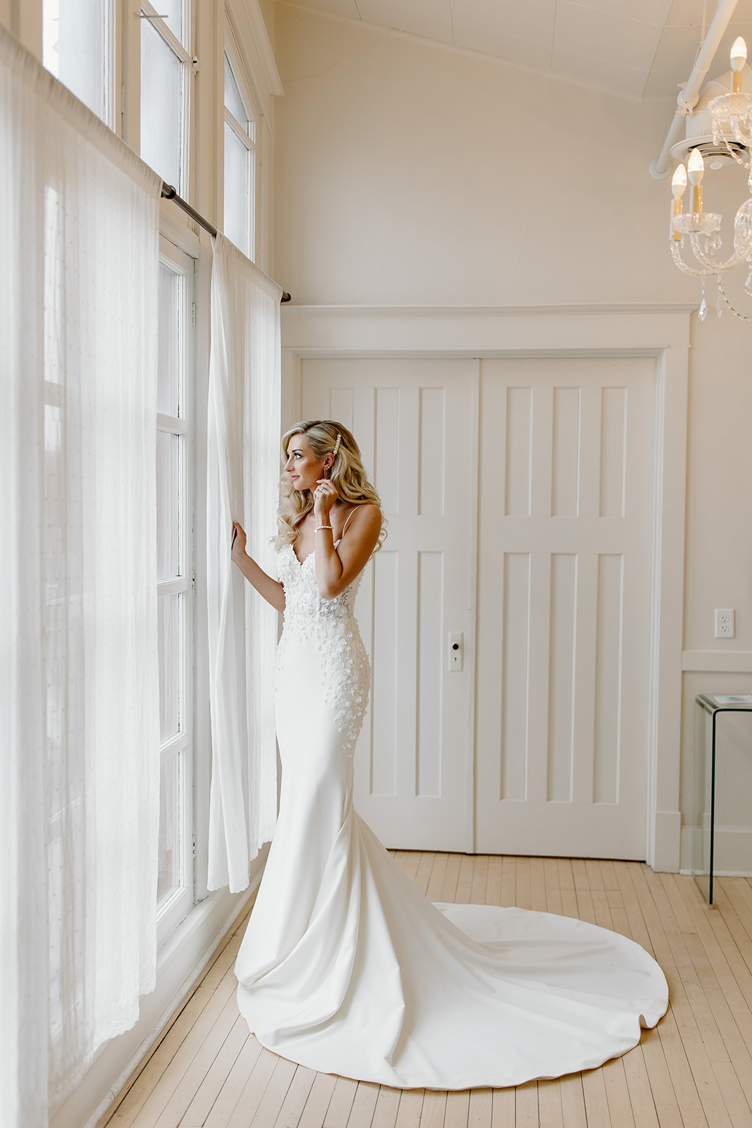 Bride standing next to a window as she gets ready on her wedding day.