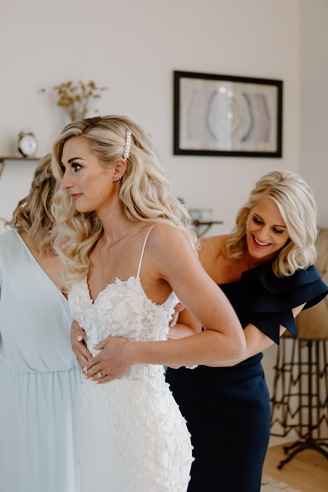 Bride's mom and sister zip up her wedding dress the morning of her wedding day.
