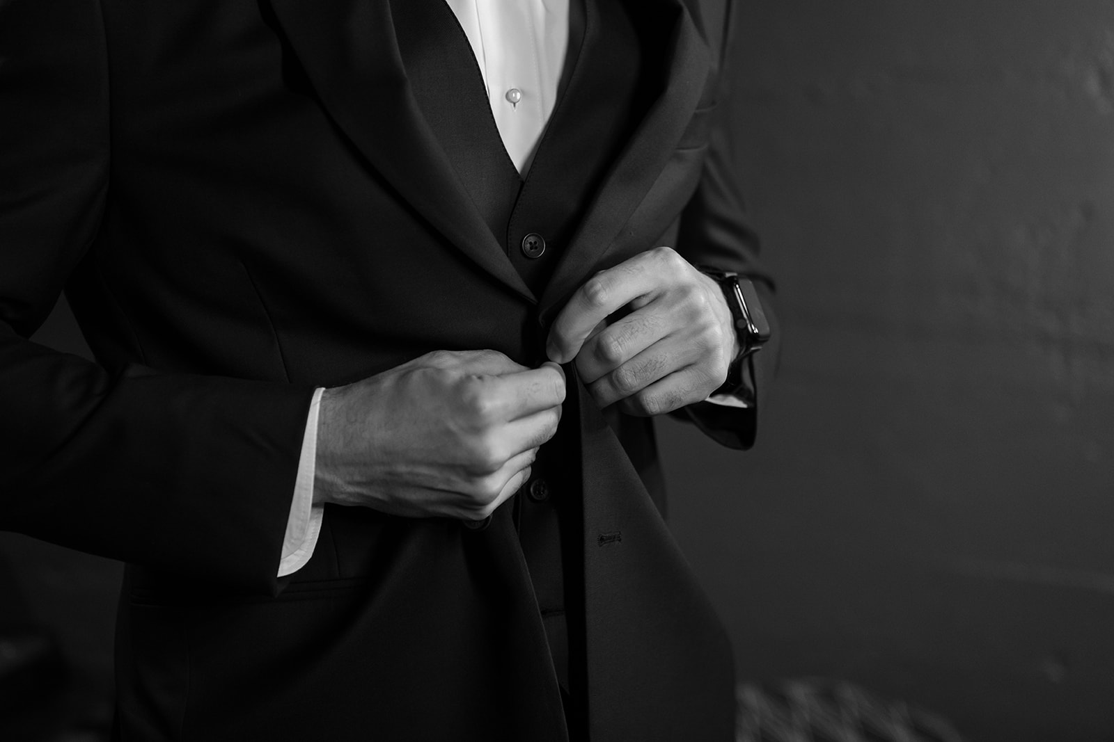 A close up of the groom's hands as he buttons up his jacket on his wedding day.