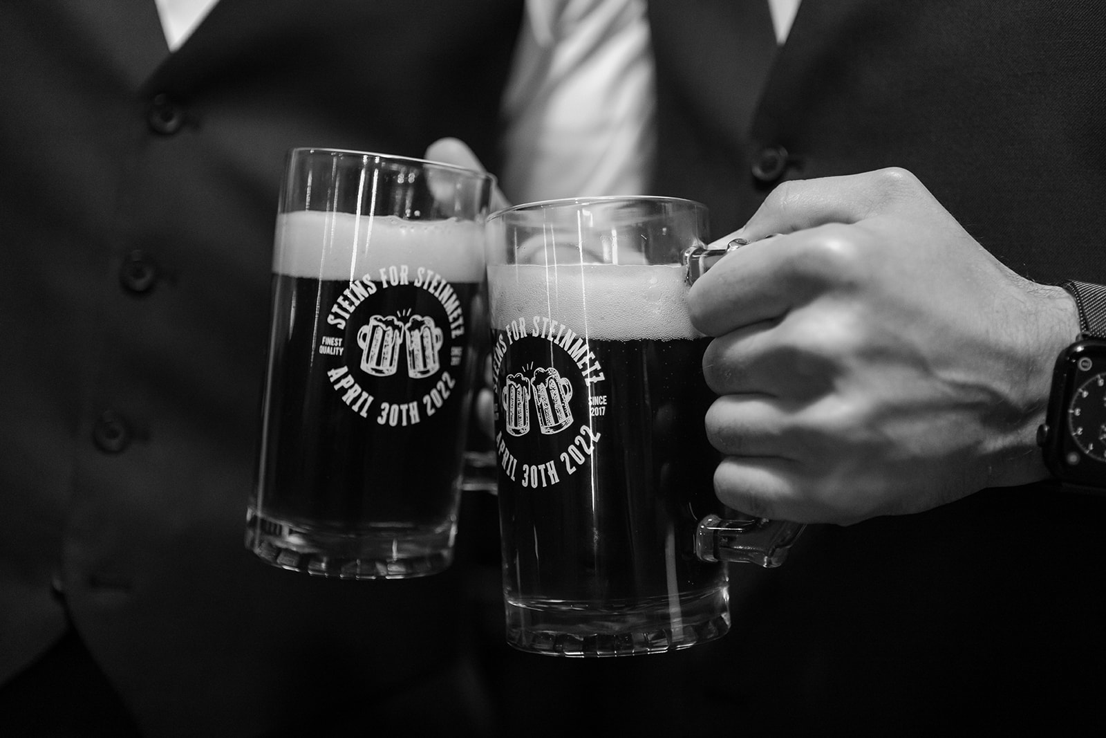 Close up of two hands cheersing steins of beer that say the bride and groom's last name.