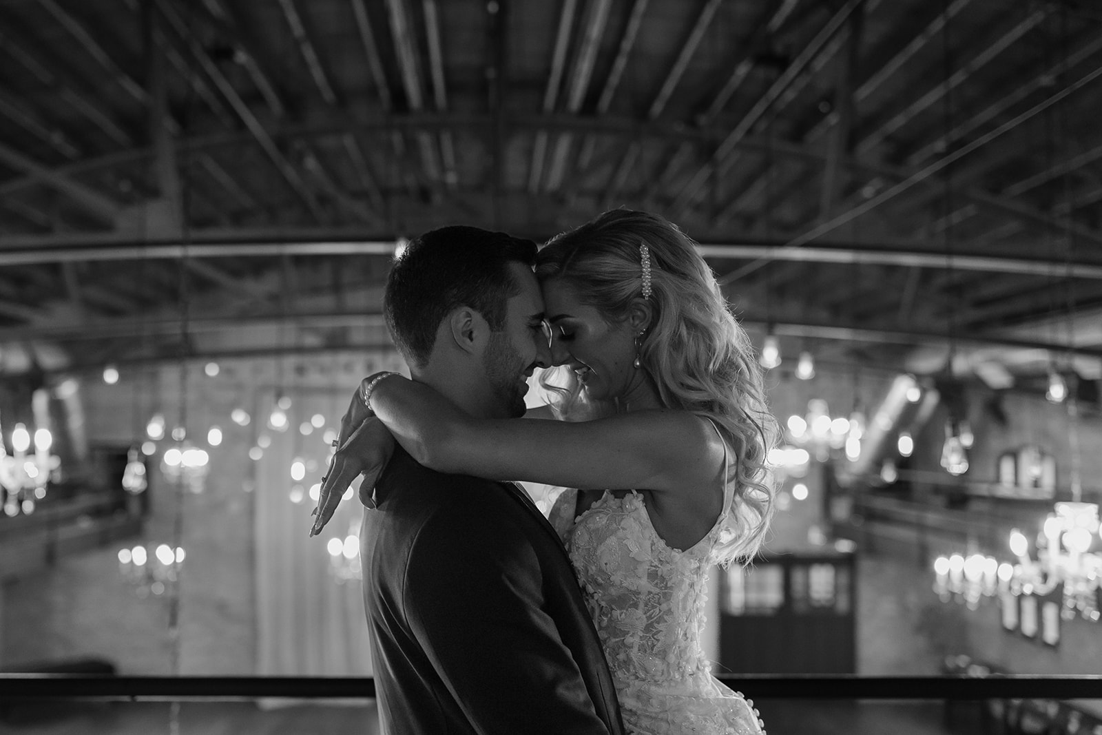 Groom holds his bride in front of a room of twinkly lights. 