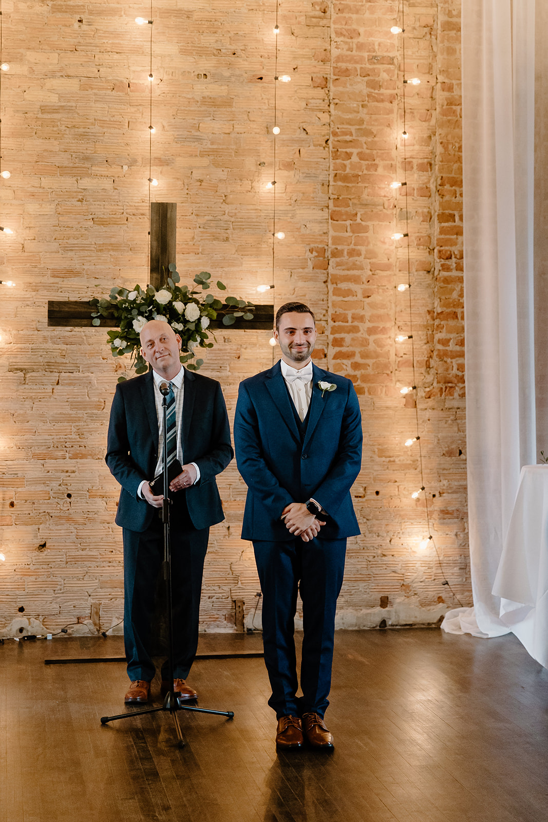 Groom smiles in front of officiant as he watches his bride walk down the aisle.