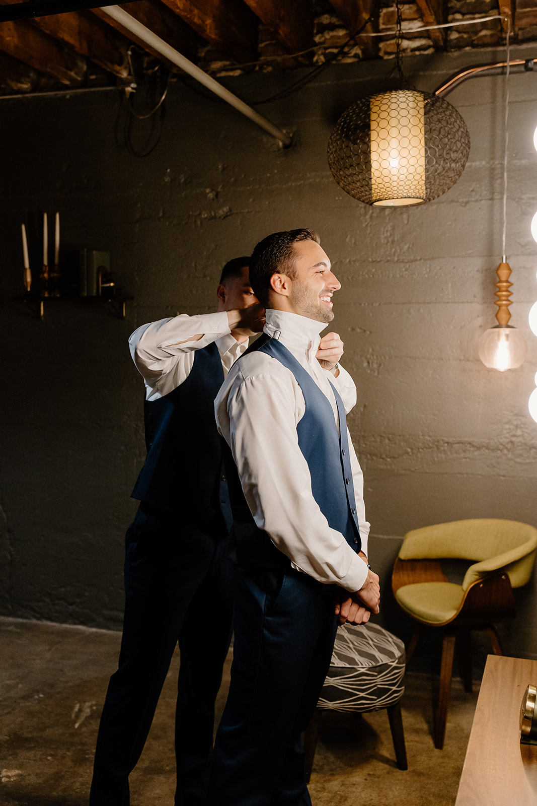 Groom smiles into mirror as his brother helps him get ready.