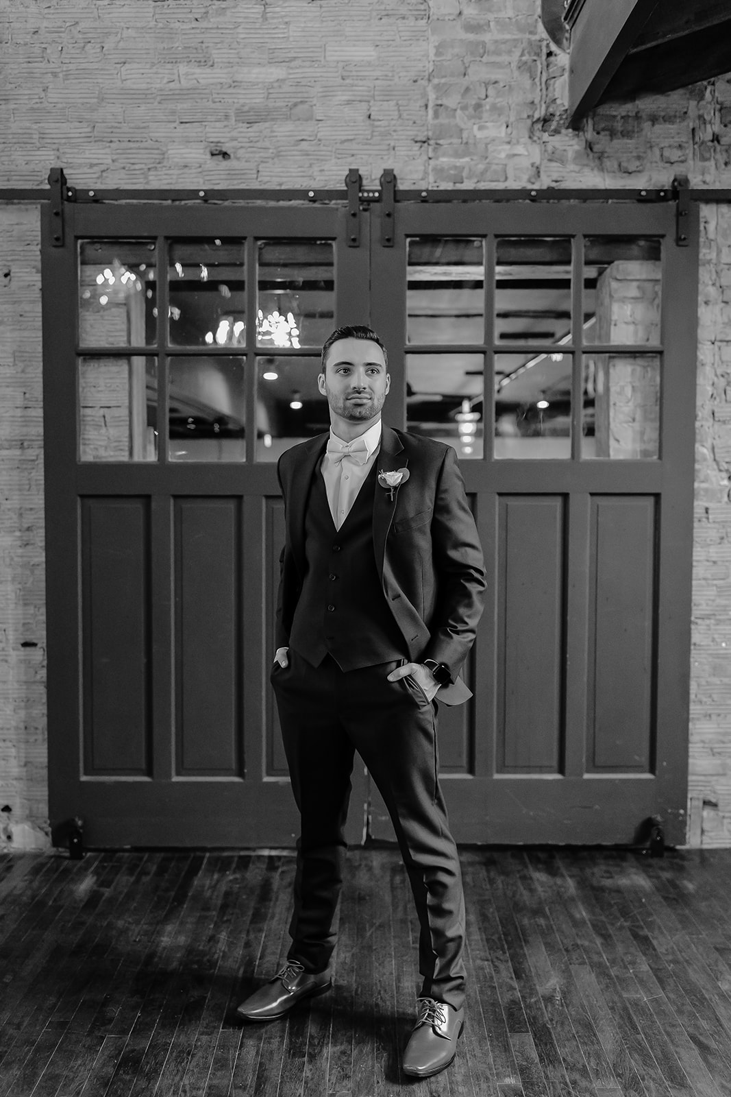 Groom stands in front of a door with twinkly lights. 