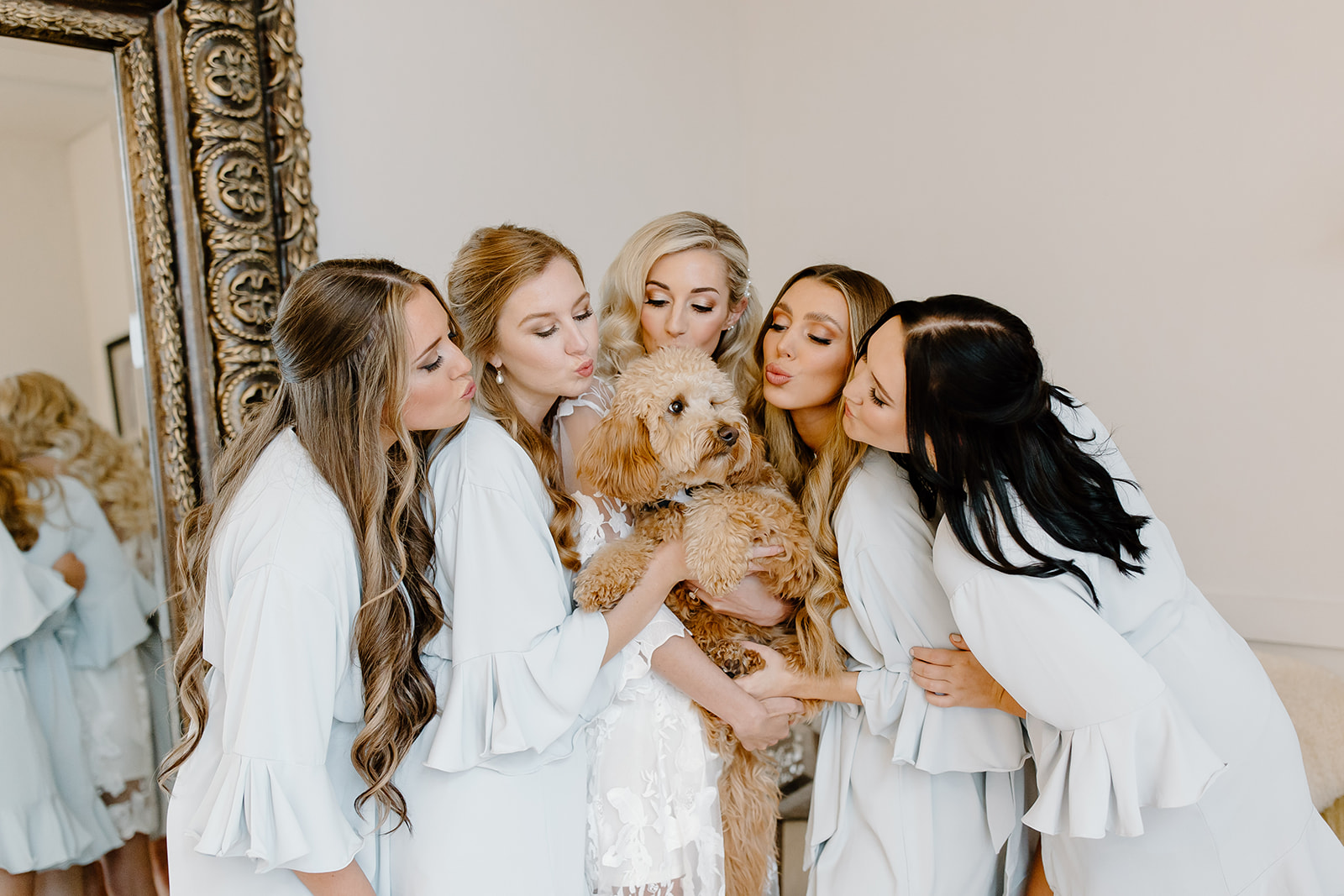 The bride and her bridesmaids kiss her mini golden doodle.
