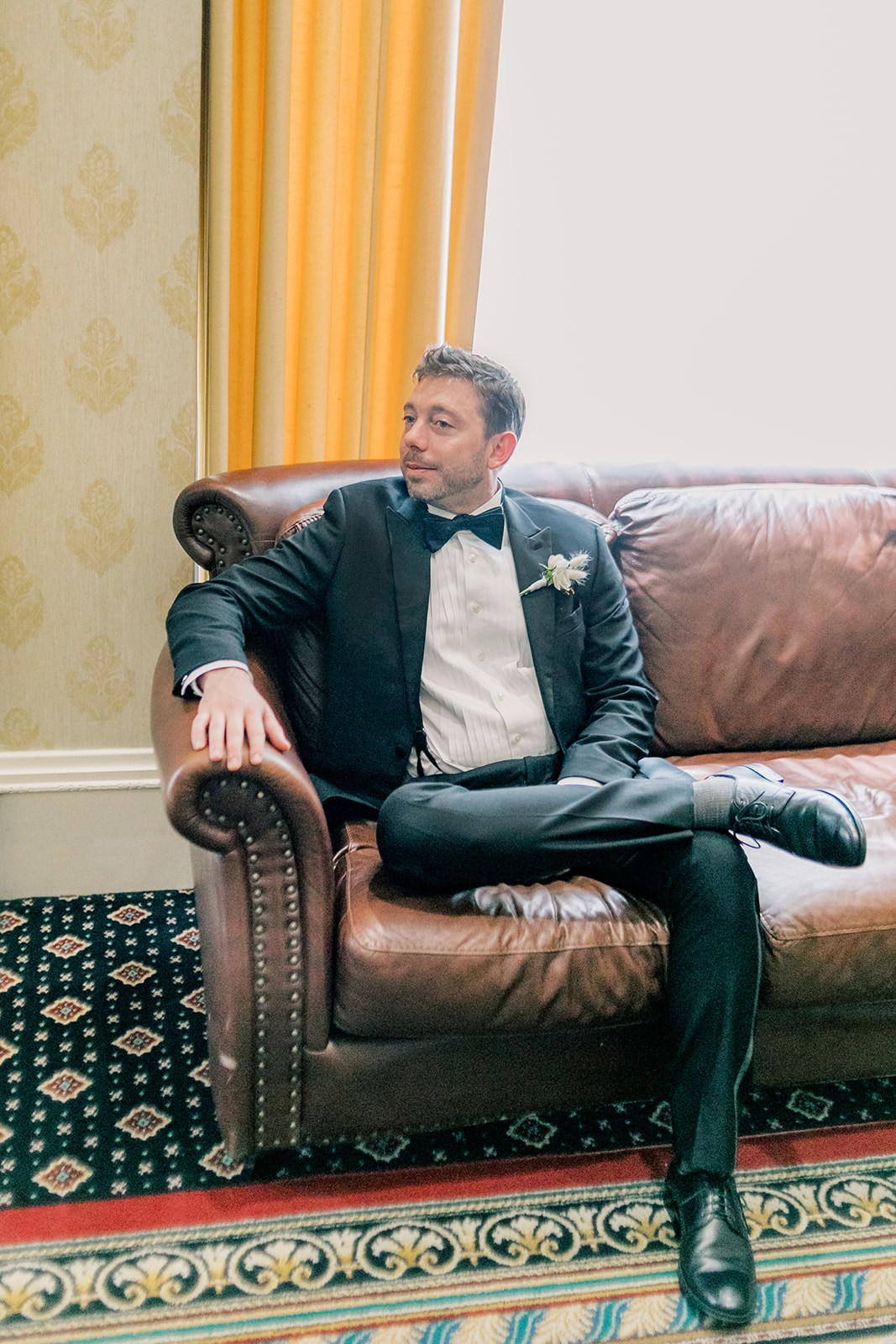 Groom sitting on sofa looking to the left. 