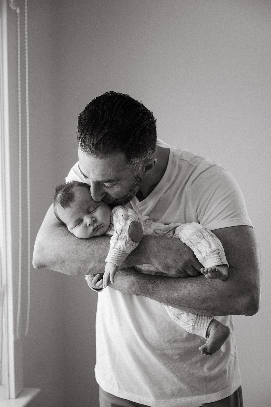Black and white photo of dad kissing his newborn baby 