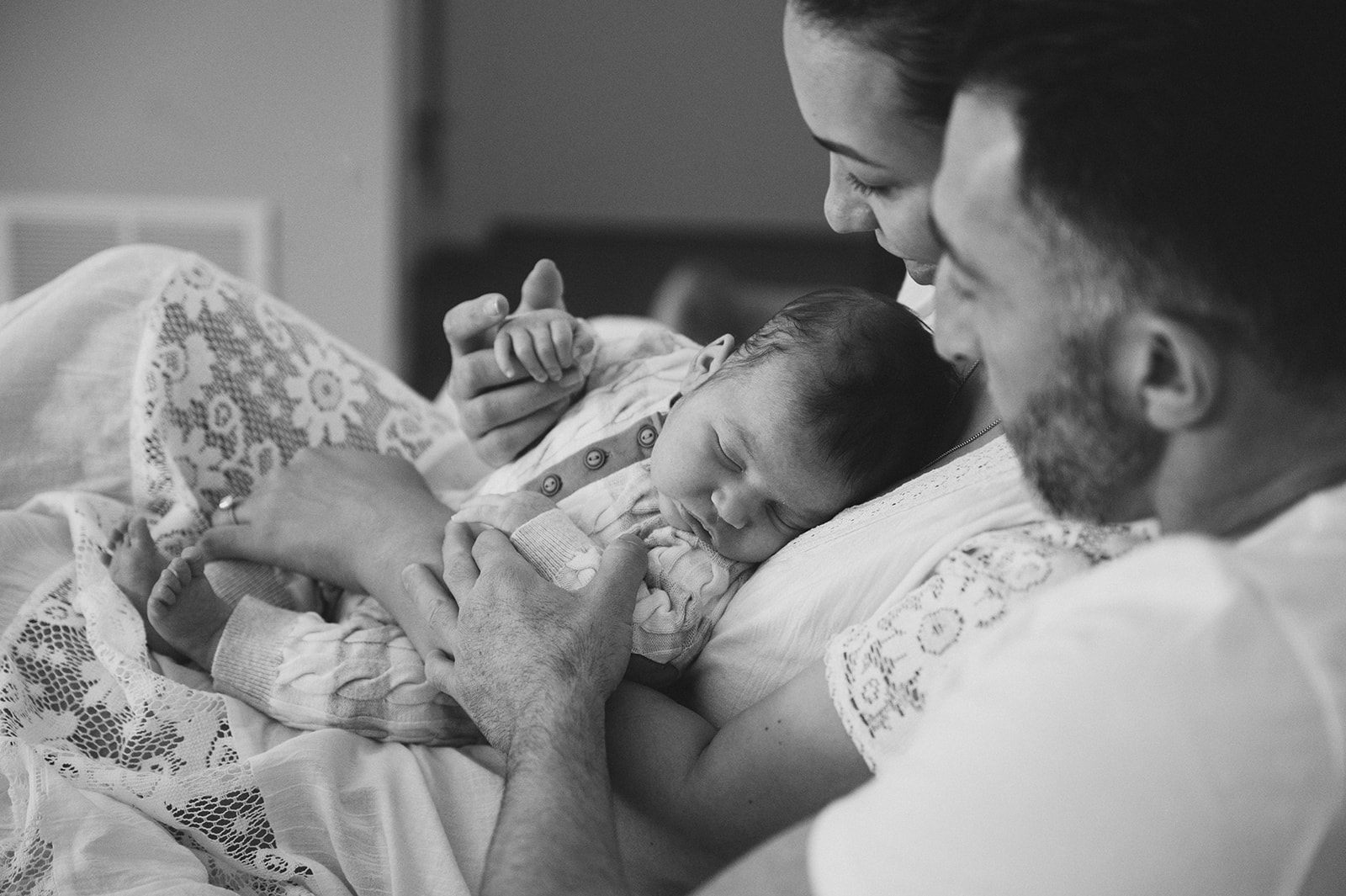 Black and white photo of new Parents in Pittsburgh, PA snuggling new baby on their bed