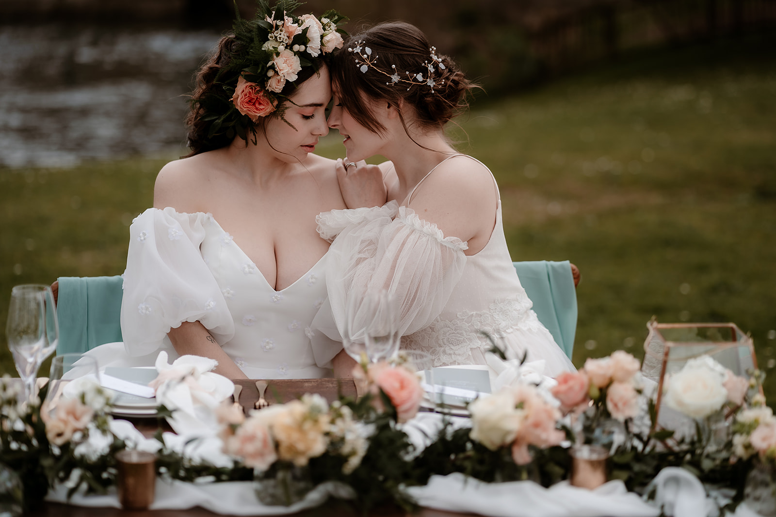 Two brides snuggle close together on their sweetheart table set up on the grounds of Mapledurham House wedding venue
