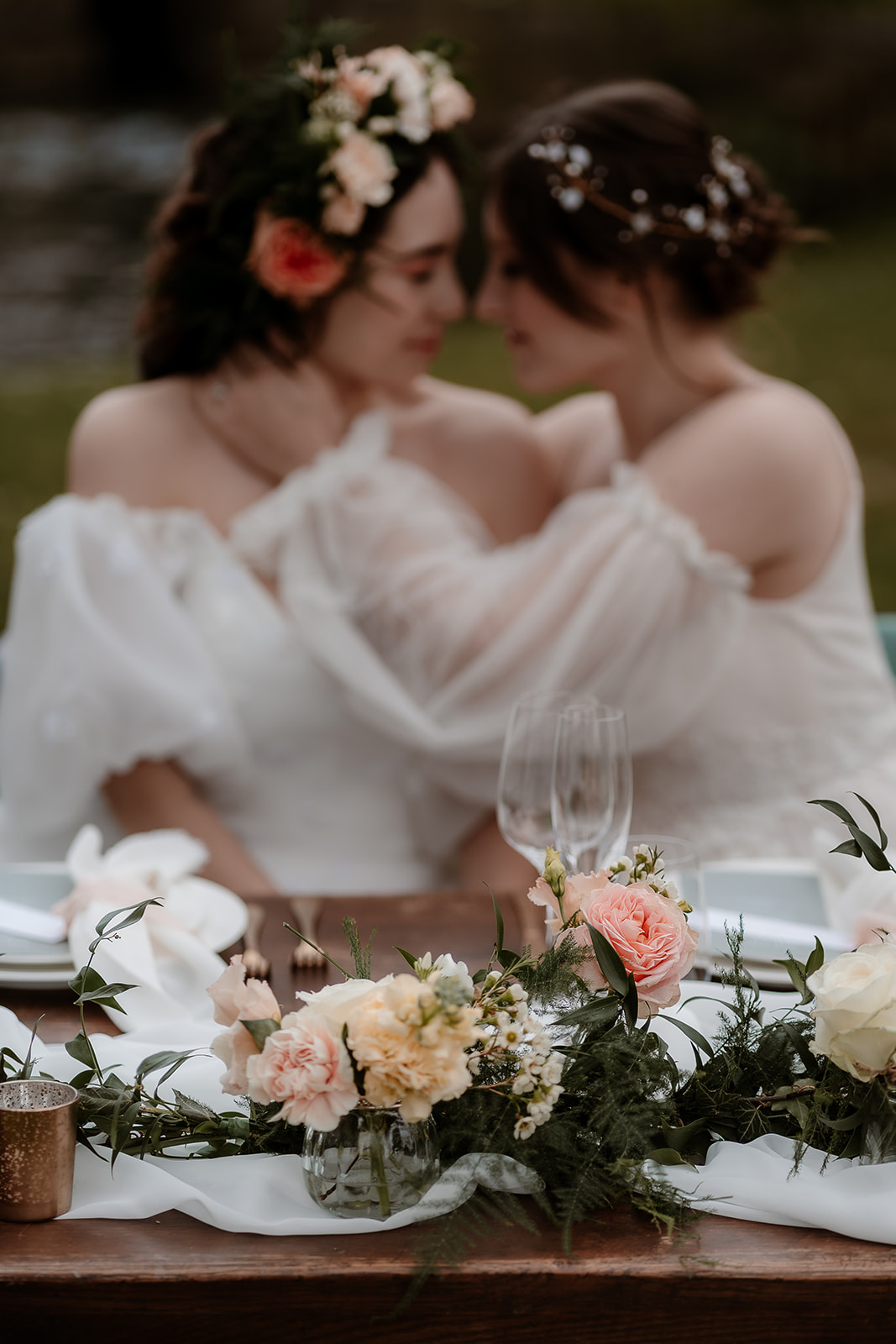 Two brides snuggle close together on their sweetheart table set up on the grounds of Mapledurham House wedding venue