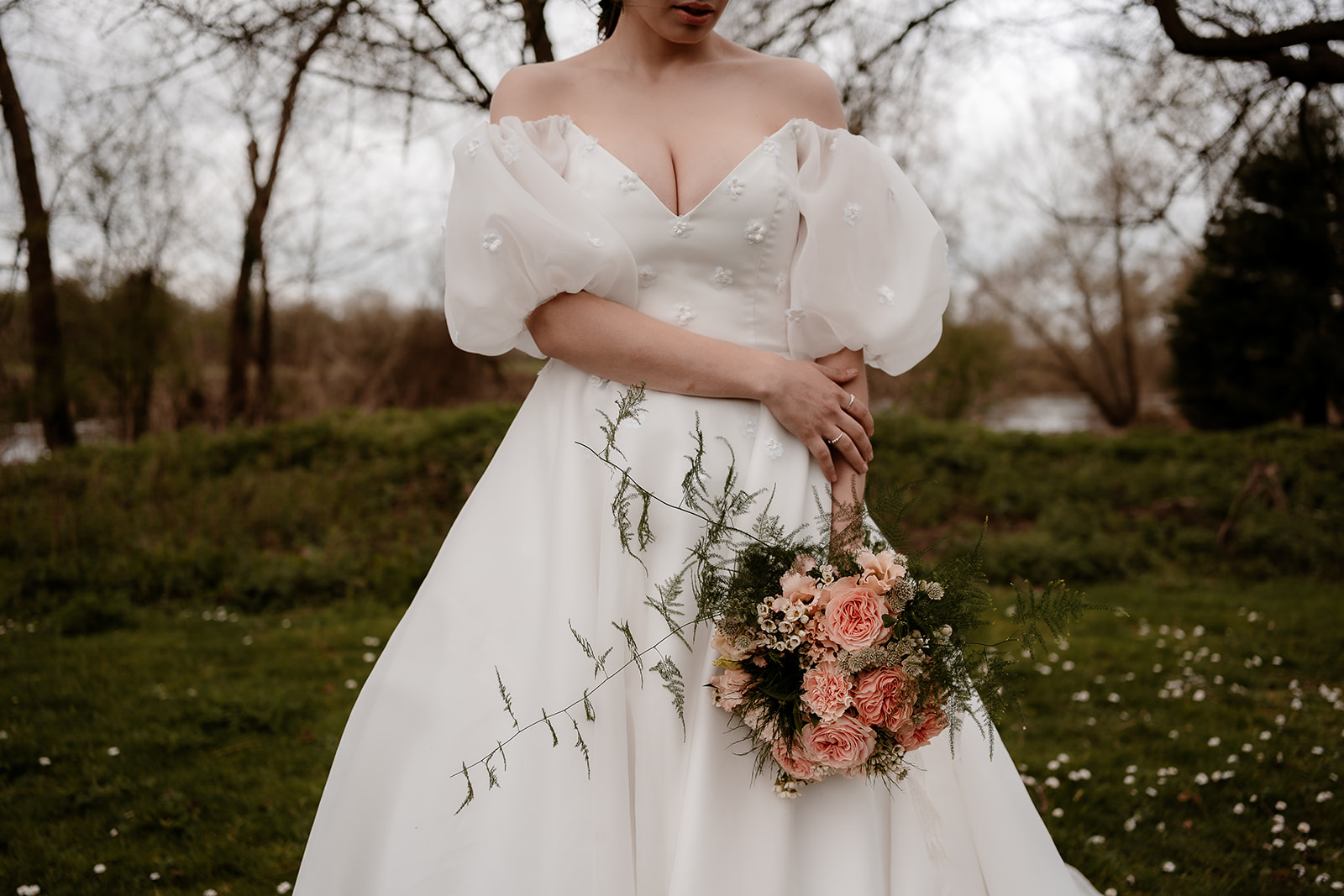 Shot of a bride's torso and arms as she stands holding her bouquet against her white dress with puff sleeves