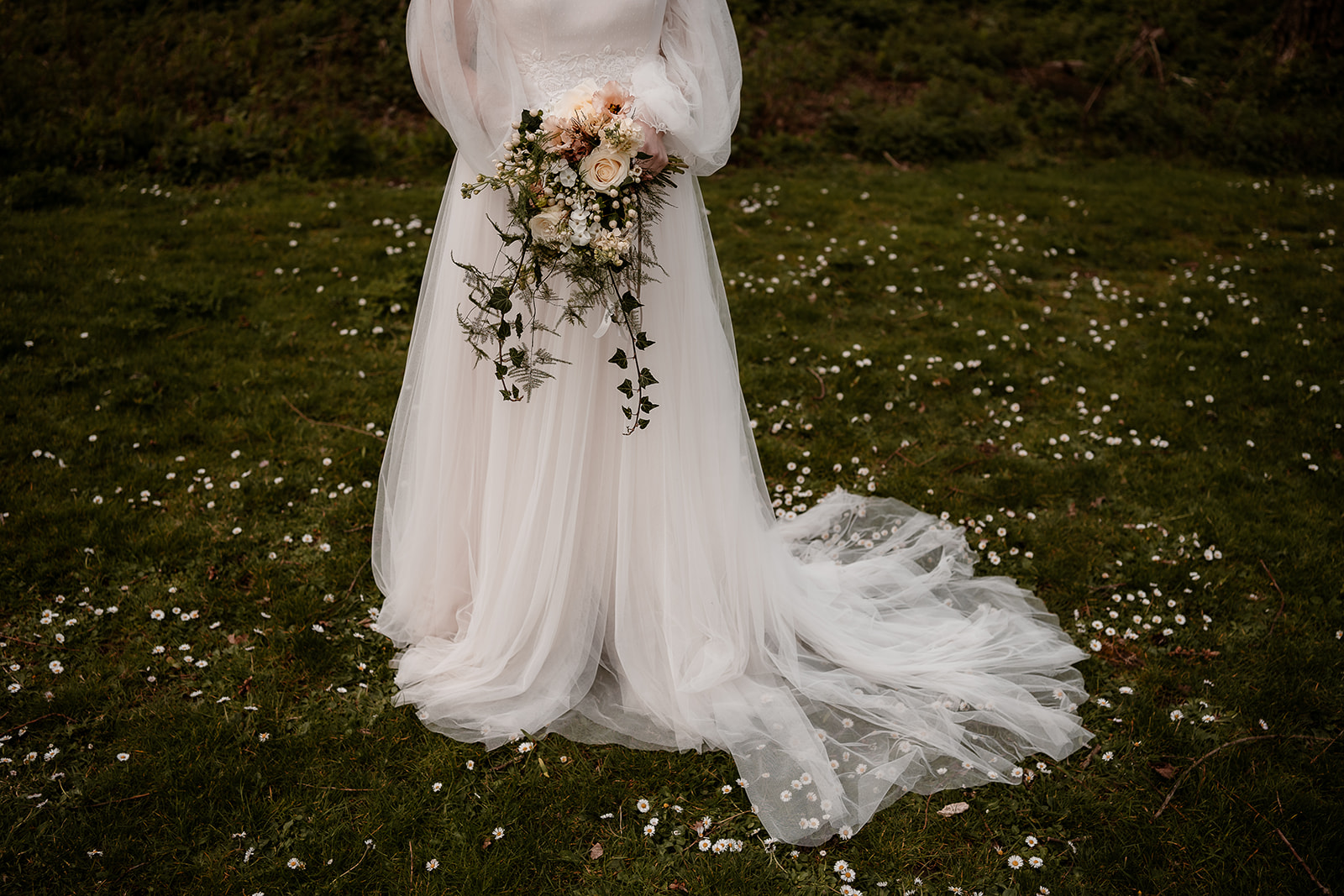 Shot of a bride's torso and arms as she stands holding her bouquet against her white tulle dress